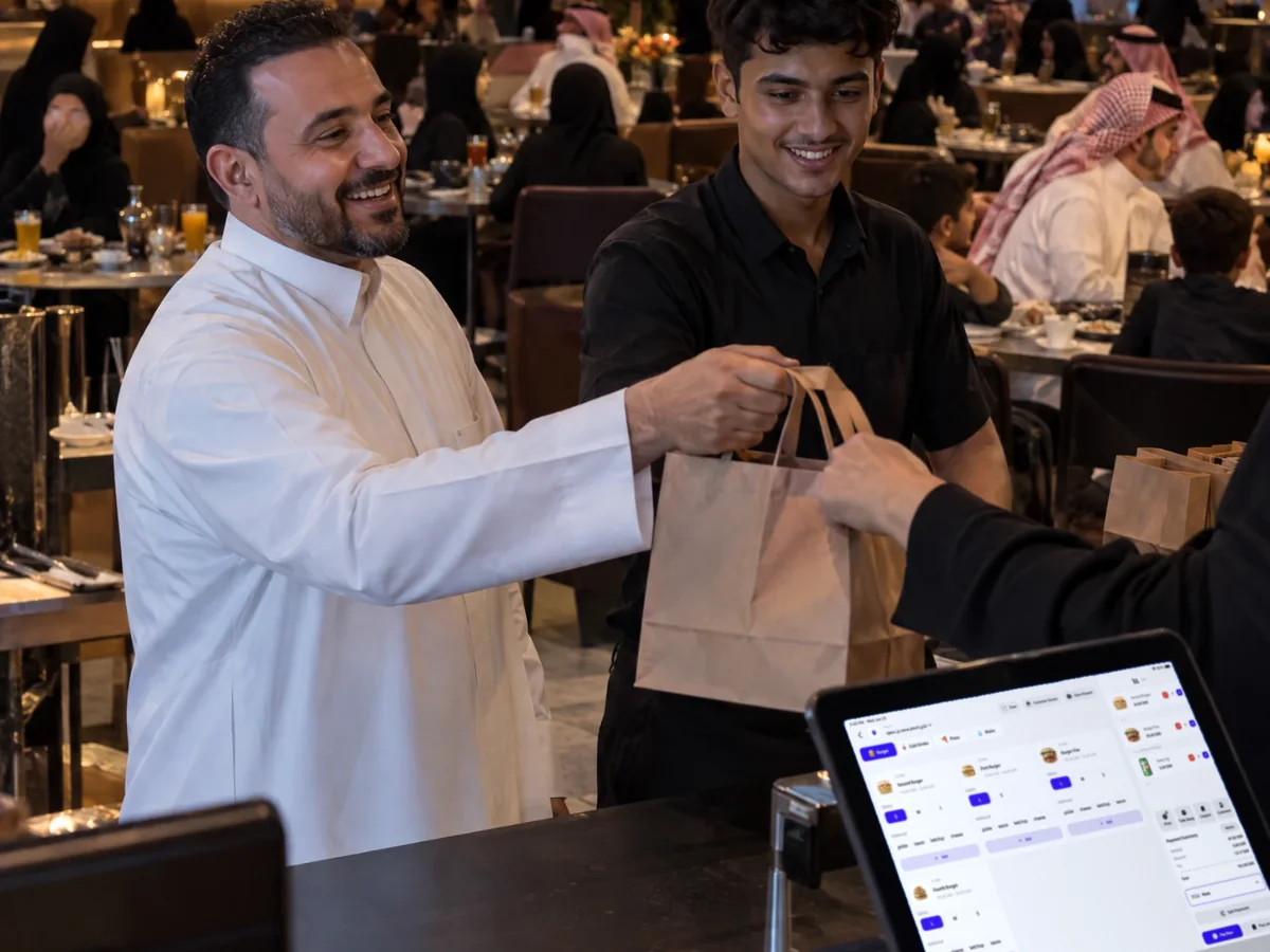 Restaurant owner handing over a takeaway order at peak time, with a QFlavours till on the counter Restaurant owner handing over a takeaway order at peak time, with a QFlavours till on the counter