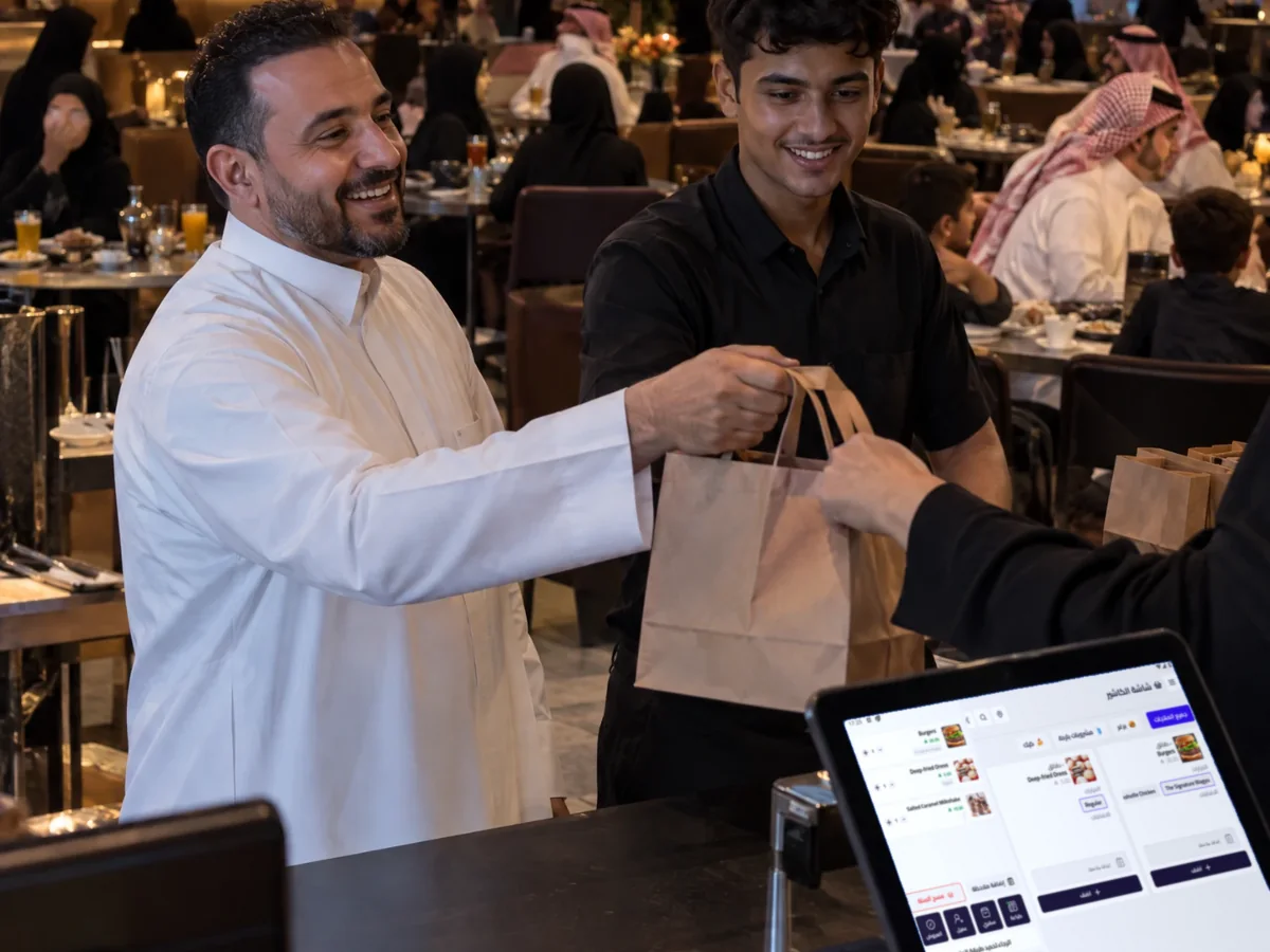 صاحب مطعم يسلّم طلباً سفرياً وقت الذروة وجهاز كاشير قيود فليفرز على الكاونتر صاحب مطعم يسلّم طلباً سفرياً وقت الذروة وجهاز كاشير قيود فليفرز على الكاونتر